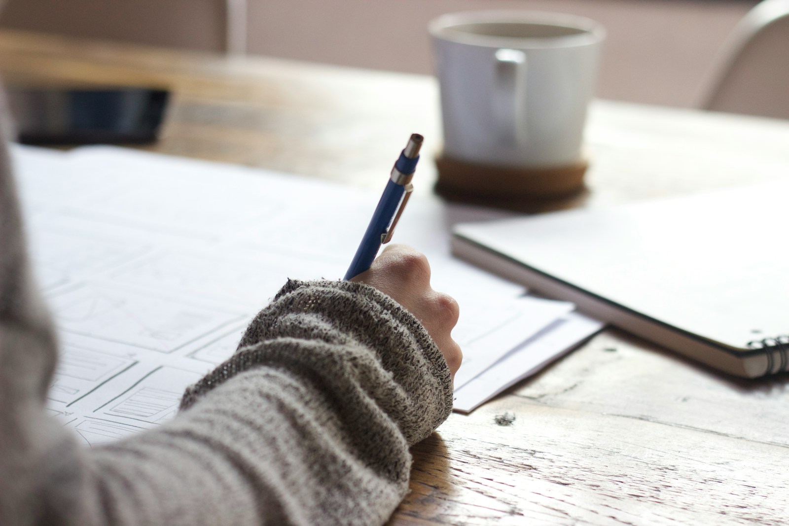 person writing on brown wooden table near white ceramic mug completing their general liability insurance